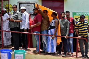 Men use a stole to cover from heat as they wait in a line outside a polling station to cast their votes in Bhubaneswar, India.